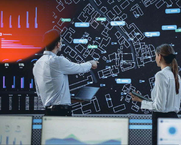 Male And Female Logistics Specialists Discussing New Routs Of Delivery In Front Of Big Digital Screen In Monitoring Office